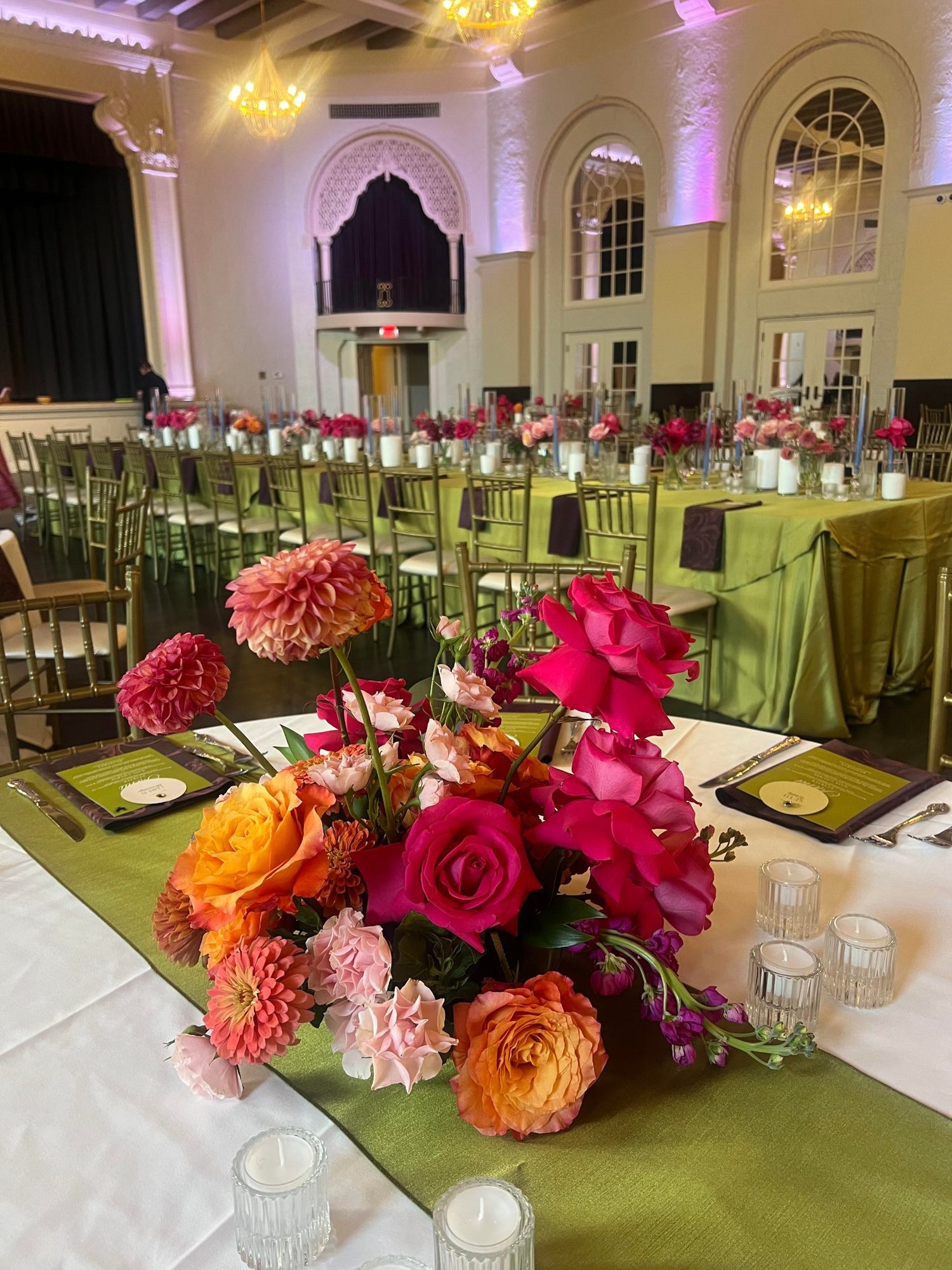Orange and hot pink roses, dahlias and stock on a green table runner in the Leo Ballroom, before the doors opened
