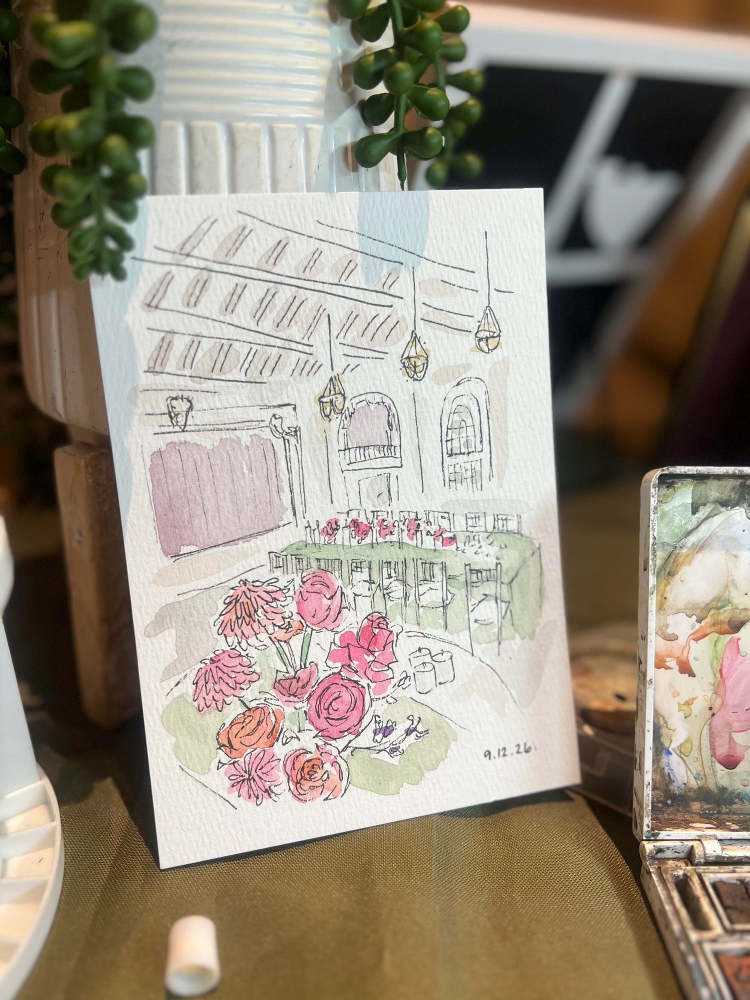 Nicole’s ink and watercolor painting of the same centerpiece and ballroom, dated 9.12.26, next to her paint palette