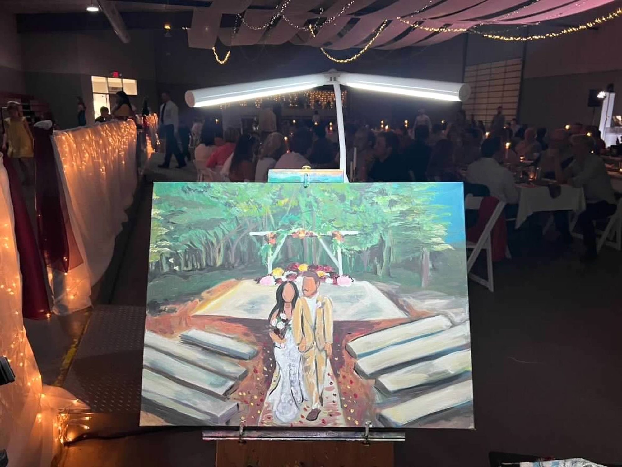 Live canvas painting of a wedding scene on an easel, glowing under the reception lights