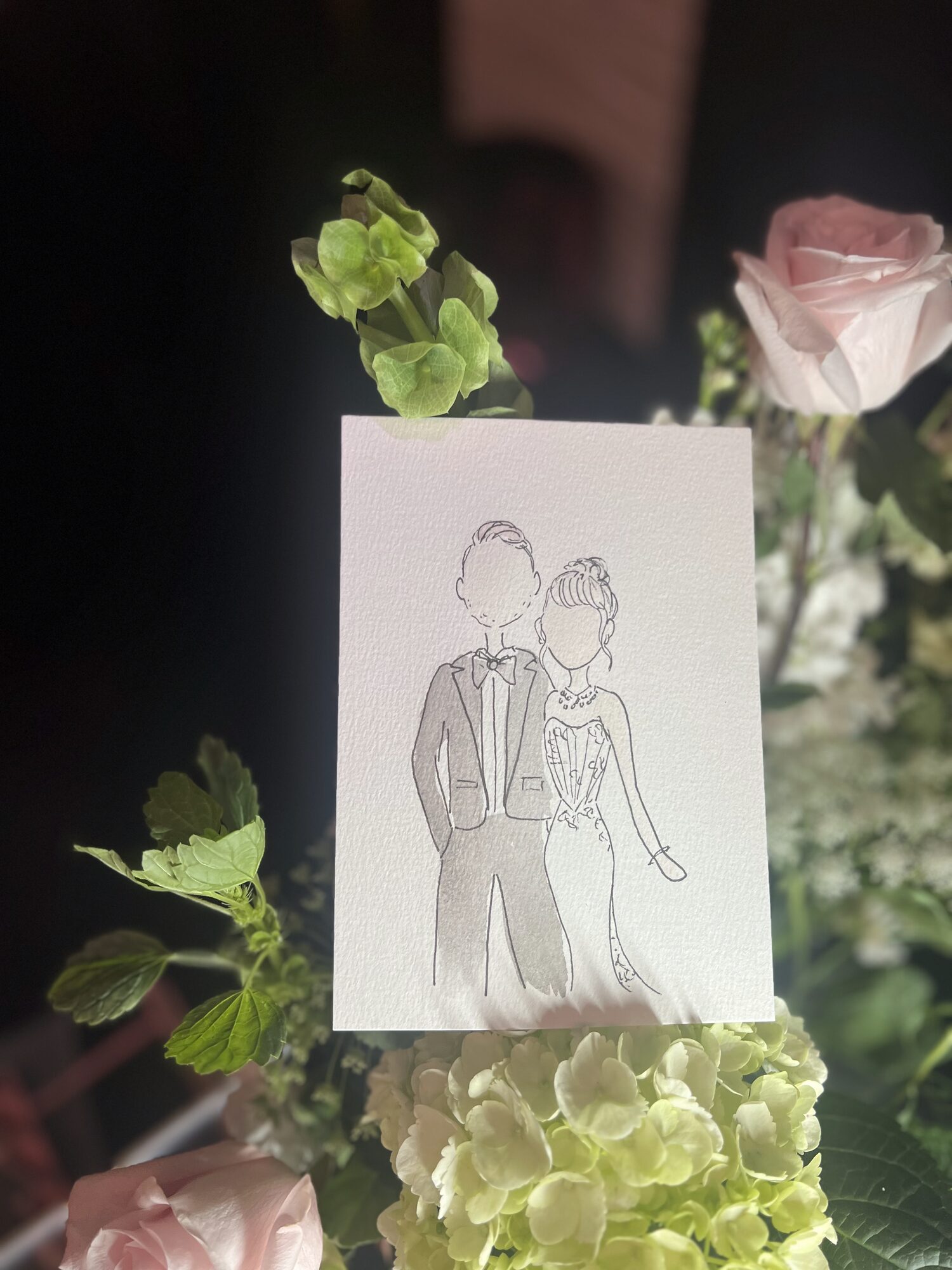 A finished mini portrait held up among roses and hydrangeas on a reception table