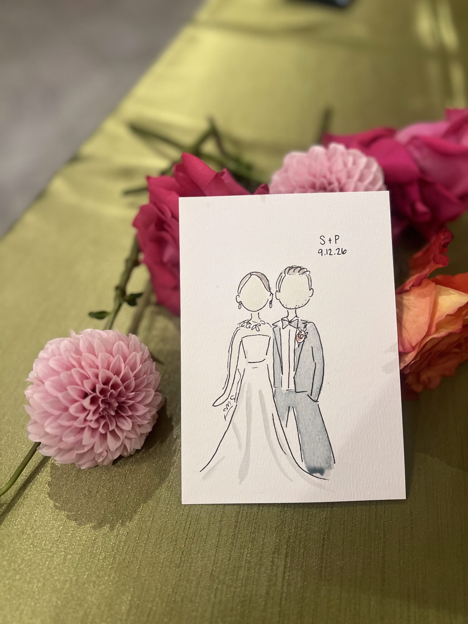 Mini portrait of a bride and groom resting on a green table runner beside dahlias and roses