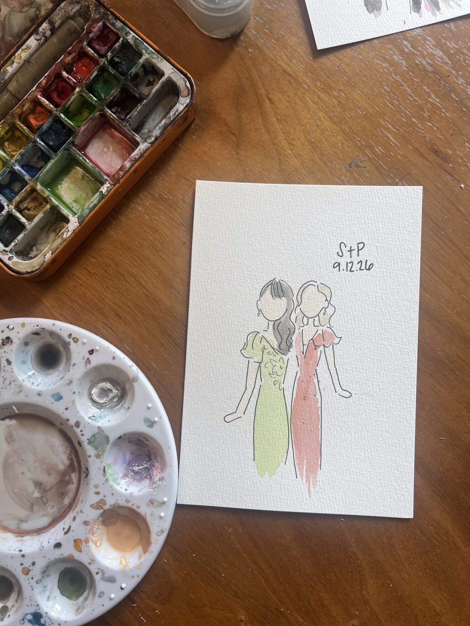 Mini portrait of two friends in green and coral dresses, next to Nicole’s watercolor palettes