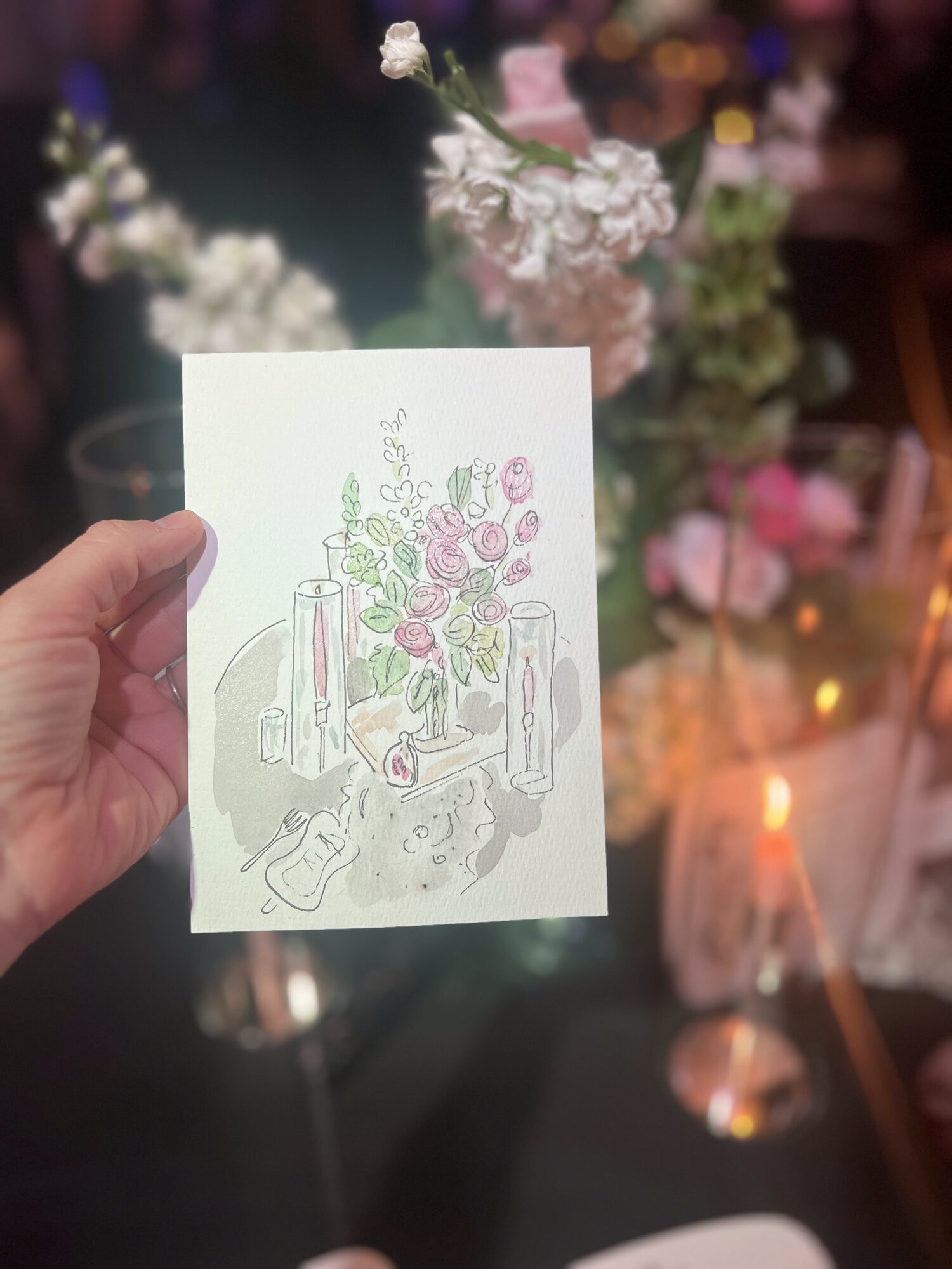 Ink and watercolor painting of a candlelit floral centerpiece, held up at the reception