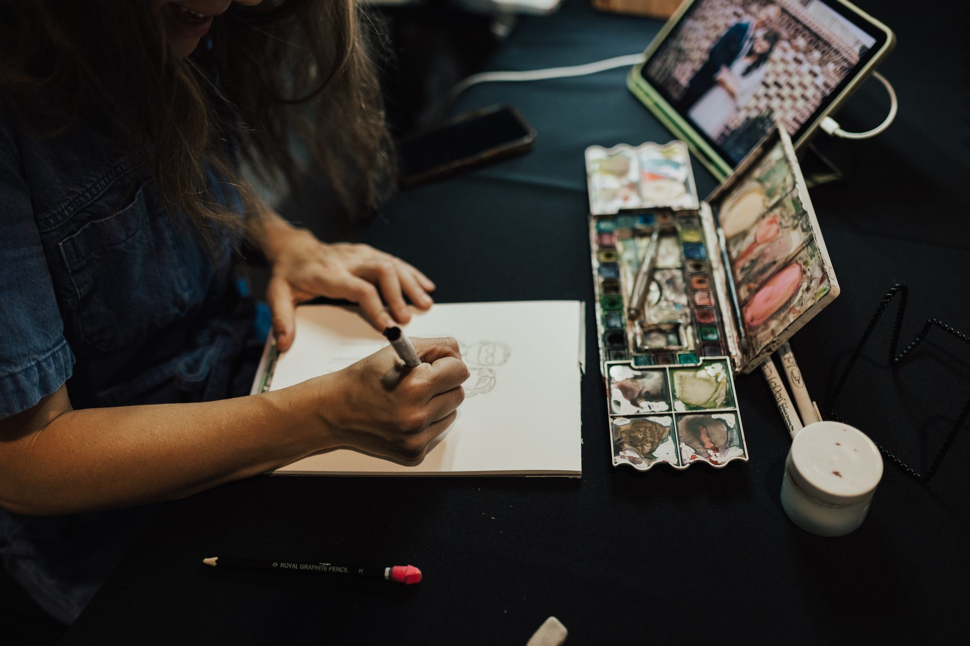 Nicole sketching at her event table, watercolor palette beside her